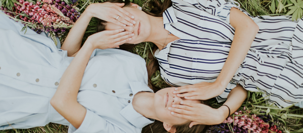 Two girls lying on glass covering each others' eyes